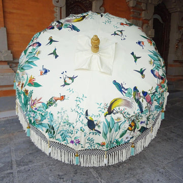 Birdie Parasol featuring exotic bird patterns on a soft white canvas, with handcrafted details and turquoise tassels.